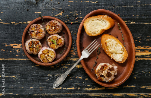 Fototapeta Naklejka Na Ścianę i Meble -  Bowl with baked garlic, thyme, rosemary and croutons on black wooden background