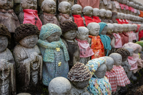 Stone Jizo statues, guardians of children, in Osaka, Japan, wear colorful knitted red hats and red bibs. A tradition offering protection and blessings.