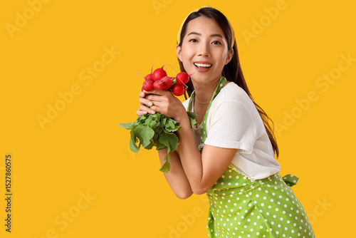 Happy young Asian housewife with ripe radish on yellow background