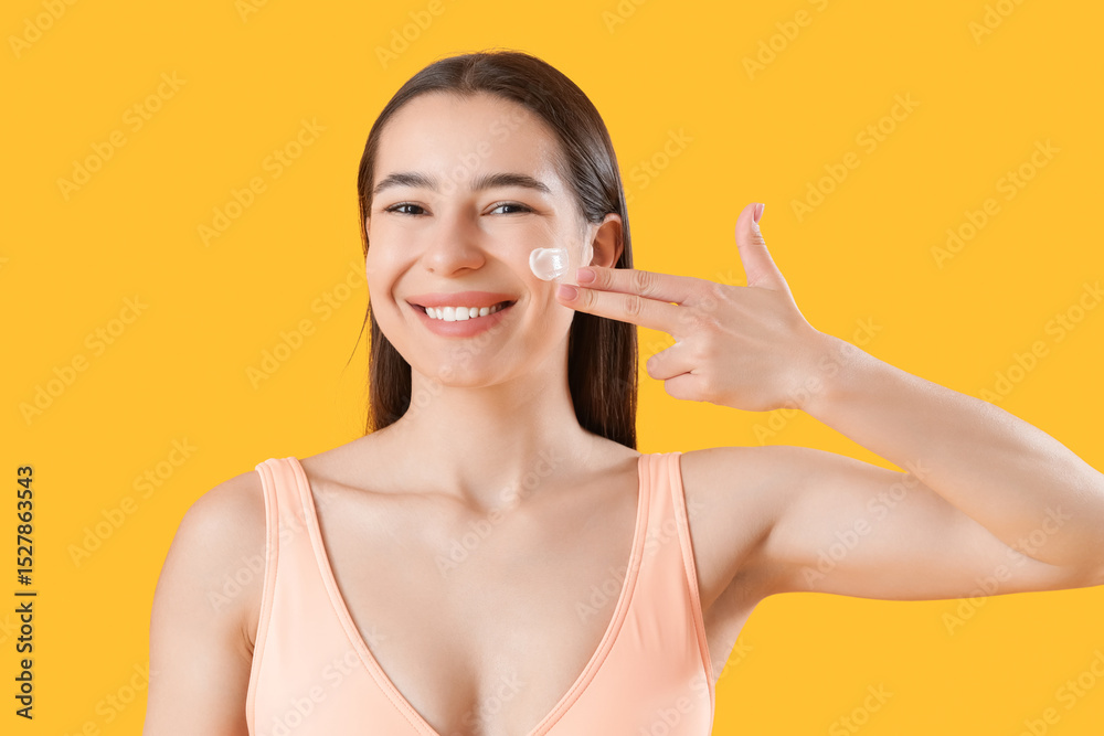 Young woman in swimsuit applying sunscreen cream on yellow background, closeup