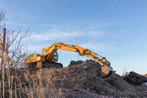 Yellow excavator groundworks on sunset, digger on construction site on blue sky. Heavy construction equipment on excavation on construction site, open-pit mining photo