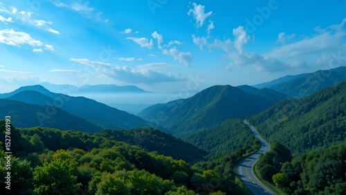 Scenic mountain range with lush green forests under a blue sky, featuring a winding road cutting through the landscape.
