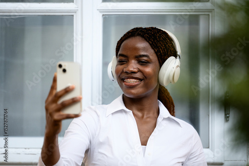 Positive black girl taking self-portrait photograph while listening to music.