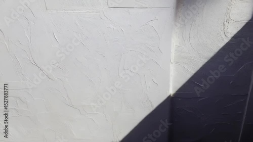 Subtle camera pan of stark white wall with textured stucco, natural light, and a shadow casting in one corner.