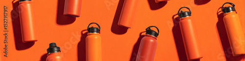 An overhead shot of various orange and red reusable water bottles on an orange colored background