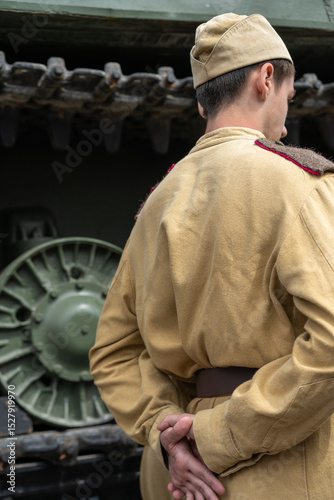 Soldier in a historical uniform stands near a tank at a World War event in a museum setting during the day