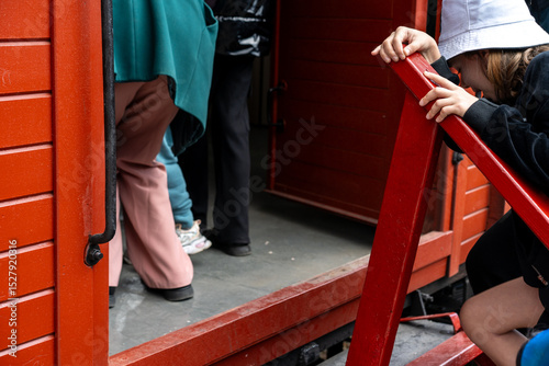 Children interact with bright red wooden structure during playful activity at community event in afternoon light