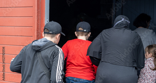 Children and an adult enter a building wearing casual clothing on a cloudy day