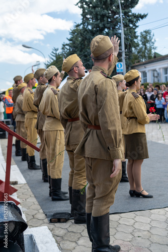 Soldiers in historical uniforms participate in a commemorative event in a town square during summer festivities