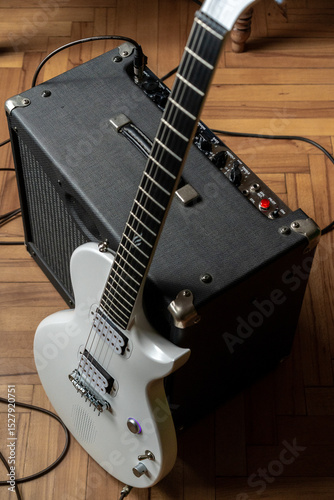 Electric guitar rests next to amplifier on wooden floor, showcasing musical setup in a casual practice space