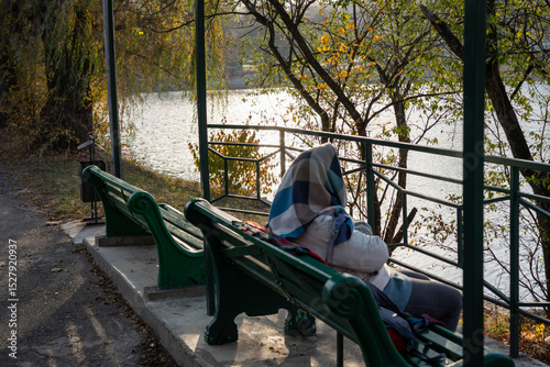 Person sitting quietly on a park bench near a lake during autumn afternoon