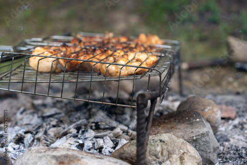 Grilling chicken on an open fire at a campsite in the forest during the afternoon