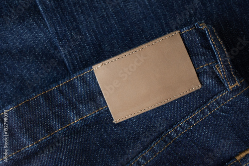Empty leather tag or label on blue denim jeans clothes top view. Shopping, sale and fabric industry background.