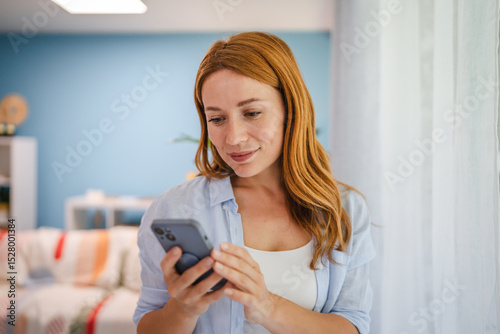 beautiful adult redhead woman stand and use mobile phone at home
