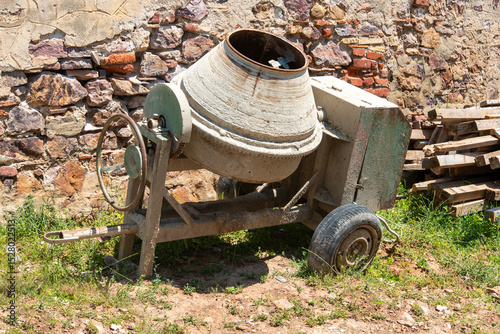 Old cement mixer sits abandoned next to a textured wall in a construction area during midday