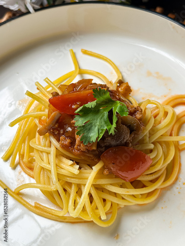A serving of spaghetti adorned with a rich tomato-based sauce, garnished with fresh herbs. Presented on a white plate, it showcases the delicious combination of Italian-inspired flavors and textures.