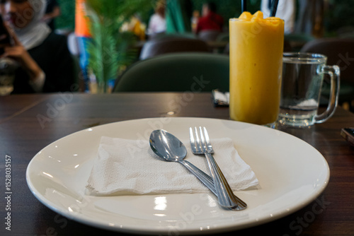 A dining plate with utensils and a refreshing drink on a wooden table at a cozy café. 