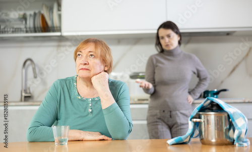 Distressed mature woman after a conflict with her daughter sitting at the table in the home kitchen