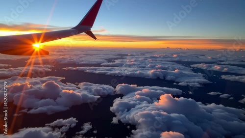 An airplane wing is seen above a sea of fluffy clouds at sunrise, with golden sunlight streaming through.