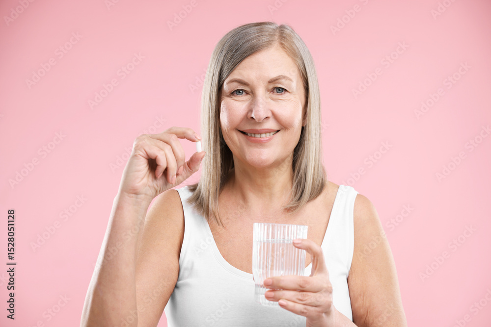 Smiling woman with collagen pill and glass of water on pink background Smiling woman with collagen pill and glass of water on pink background