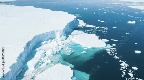 Aerial drone footage of a turquoise melt pool along sharp glacier cliffs, with floating ice fragments forming natural concentric patterns. The orbiting top-down camera circles smoothly