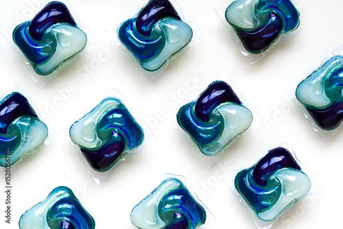 Vibrant blue and green laundry detergent pods arranged in a seamless pattern on a white surface. Concept of clean clothes, eco care, and selective focus.