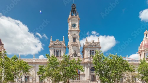 Valencia City Hall (Ajuntament de Valencia) timelapse hyperlapse in Plaza de Ayuntamiento. Historic building with clock tower under a blue cloudy sky. People strolling the main square in Spain