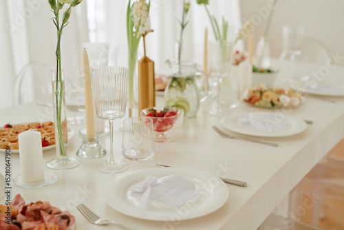 Wedding celebration table set with elegant glassware, plates, candles, floral arrangements and assorted appetizers, closeup showing place cards and festive food presentation