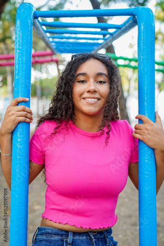 Young woman holding monkey bars at playground smiling at camera