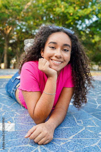Young latin woman lying on the ground smiling in a park