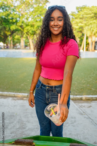 Young woman throwing plastic cup in a public trash can