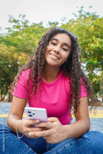 Young latin woman using mobile phone sitting in a park