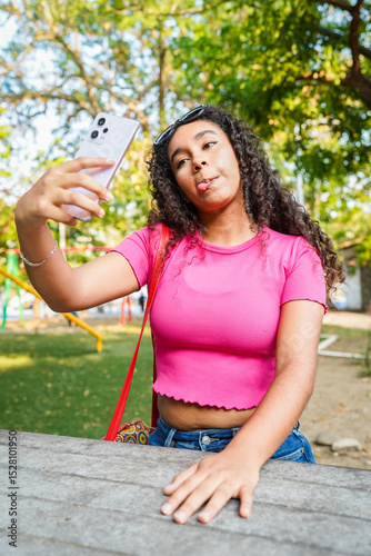 Young woman taking a selfie sticking out her tongue in a park