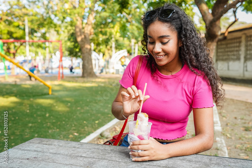 Young latin woman enjoying a refreshing shaved ice dessert in a park