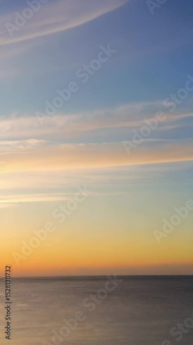 Calming morning view of the ocean with soft orange sunrise and atmospheric clouds above the water surface.