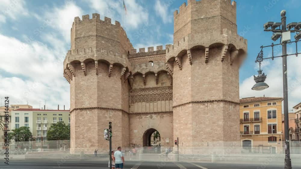 Serrans Towers (Torres de Serranos) timelapse hyperlapse in Valencia, Spain. A grand medieval gate from the city's ancient walls. Bustling street scene under a cloudy sky frames this historic landmark
