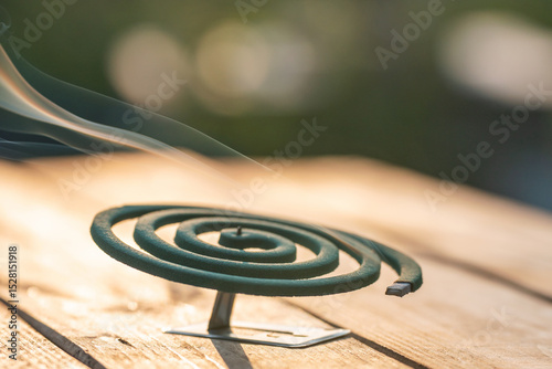 Smoldering mosquito coil in summer garden on wooden table, insect protection