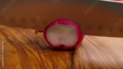 A closeup or macro shot of a sharp kitchen knife carefully slicing a fresh red radish into thin rings. Preparing healthy salad ingredients for a delicious and nutritious meal