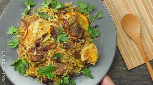 A top-down view of a person placing a gray plate filled with freshly made, aromatic beef biryani on a table. This image captures the moment of serving a delicious, traditional homemade meal