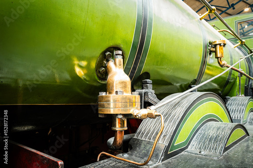 Shallow focus of a brass, steam valve fitting on a green painted, old steam powered locomotive within a, North Yorkshire railway museum. The high pressure brass relief valve can be seen.