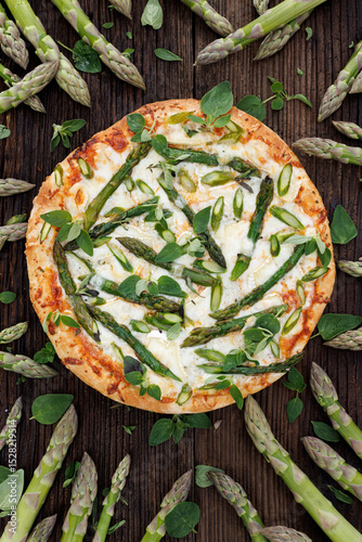 Pizza with green asparagus and herbs on a wooden background, top view