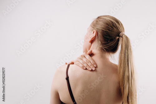 Woman with long hair is experiencing shoulder pain while holding her neck, showcasing discomfort and the impact of physical strain on daily life