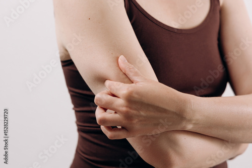 Woman in brown tank top is holding her elbow with a pained expression, conveying discomfort and the experience of physical pain in a close-up shot