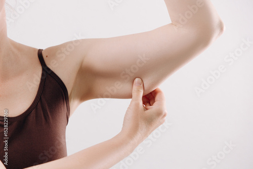 Woman demonstrating skin elasticity by pinching her upper arm, showcasing health and fitness awareness in a bright, minimalistic environment