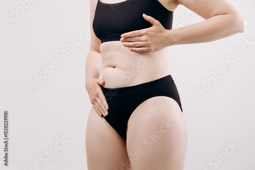 Woman in black underwear holds her stomach, expressing discomfort and pain, highlighting the emotional and physical aspects of health struggles
