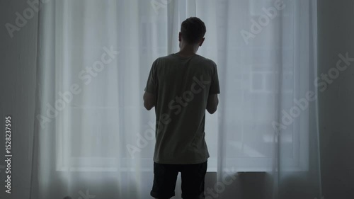 Agoraphobic man staring out the window, afraid to leave home. Mental health struggle with fear of open spaces.