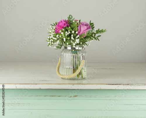 Ramo de flores blancas y rosas en florero transparente de cristal sobre mesa de madera en color pastel photo