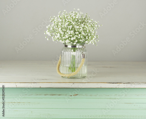 Ramo de flores blancas en florero transparente de cristal sobre mesa de madera en color pastel photo