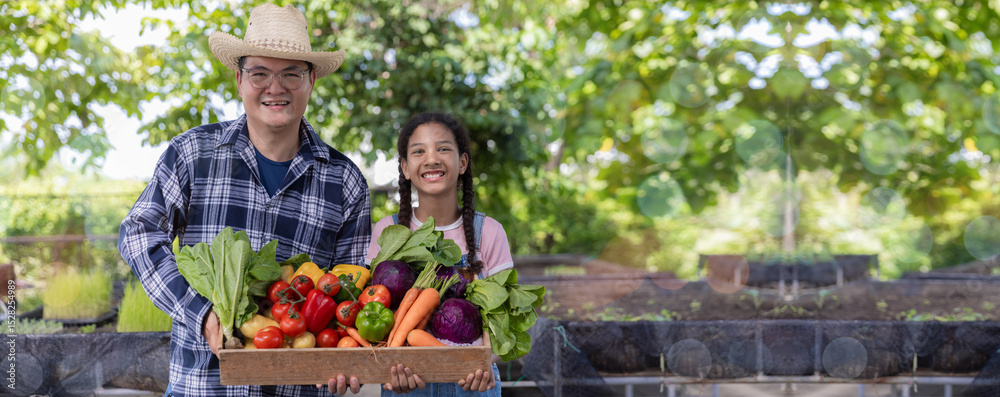 Fototapeta premium Farmer holding wooden box full of fresh vegetables. Basket with vegetable. Man and Daughter holding big box with different fresh farm vegetables.