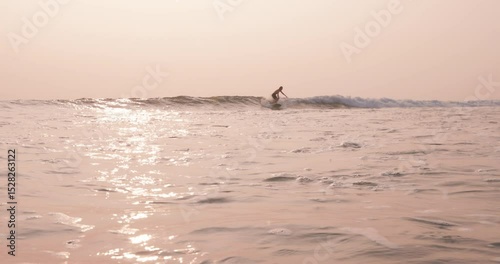 Male surfer on longboard riding on ocean wave with sunset sun light.